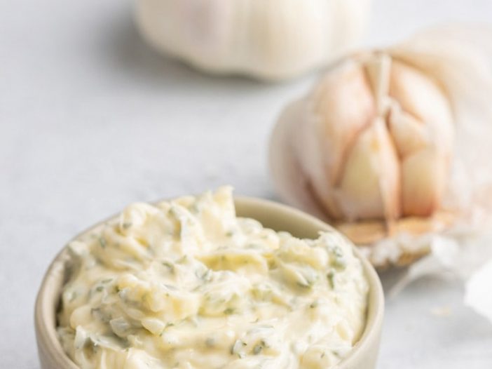 garlic butter in a small bowl, with a full head of garlic and a half head in the background
