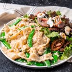 vegan alfredo pasta on a plate with salad with a beige plaid tea towel on a dark background