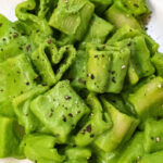 heart shaped pasta in a creamy green pasta sauce on a cream coloured plate